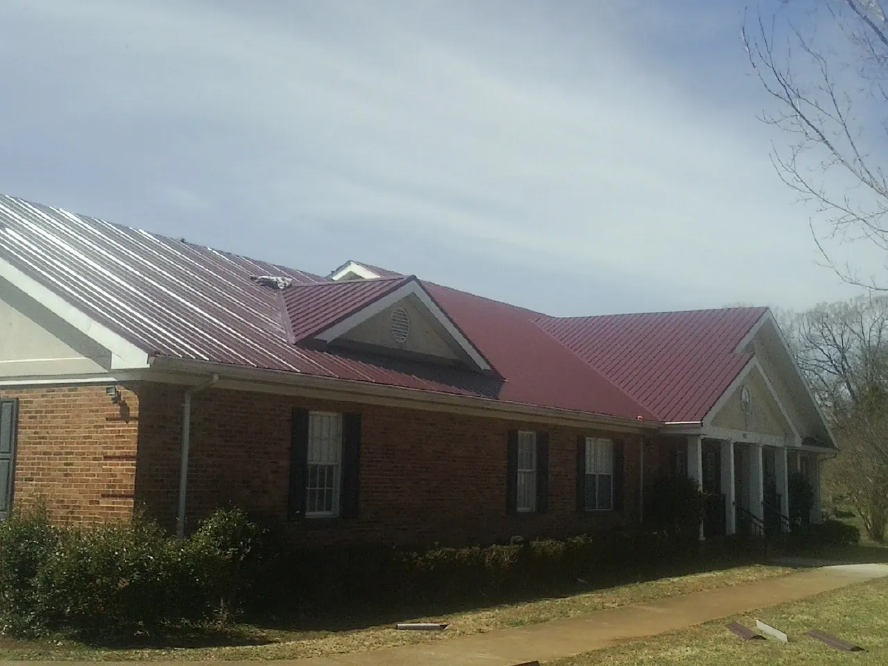 Red metal roof with gabled entries on a long brick building, from a Hail Damage Roof Repair job in Dresden